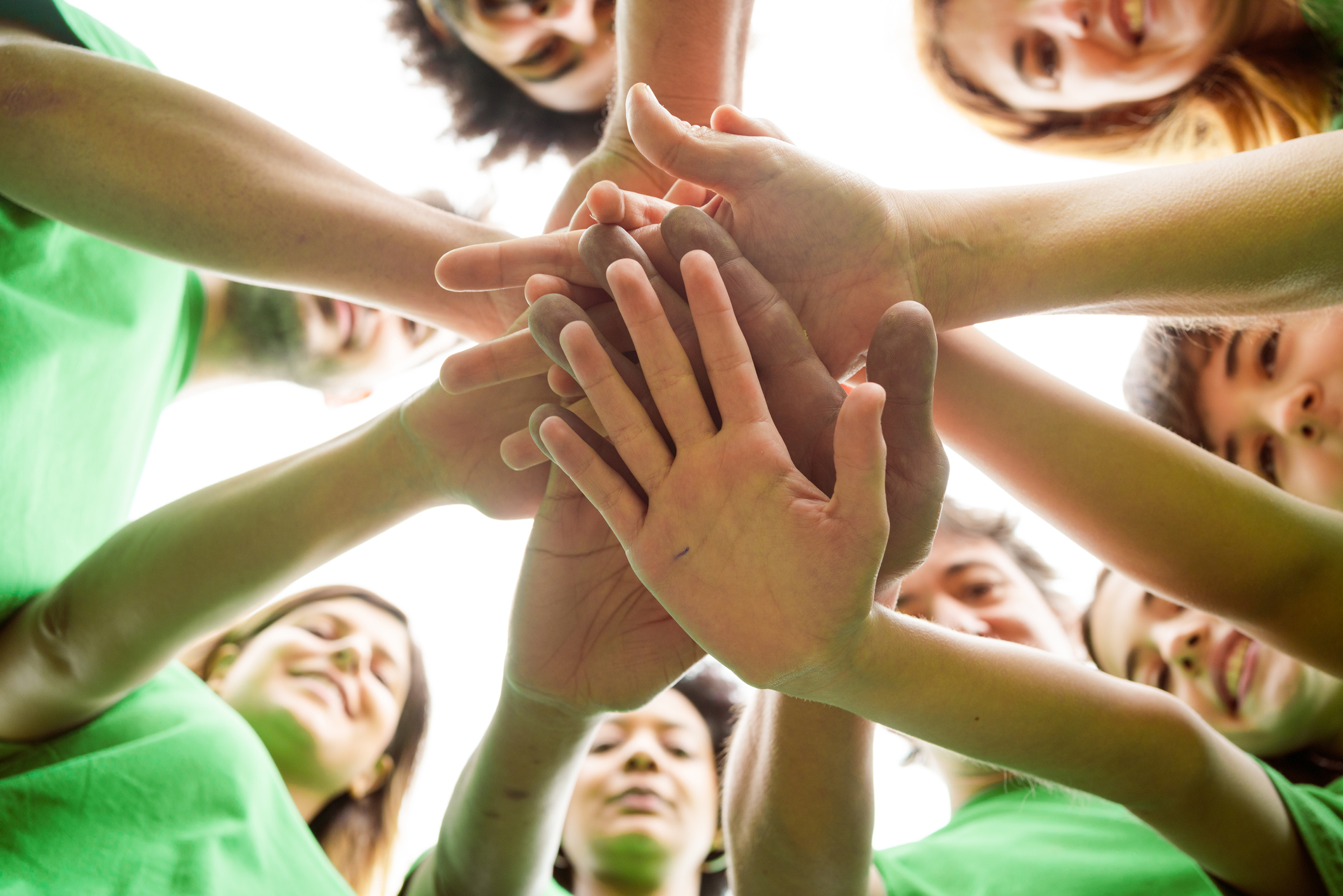 Directly below shot of volunteers stacking hands. Male and female environmentalists are in public park. They are doing environmental cleanup together.